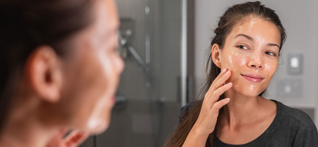 woman with cleanser on her face looking in the mirror