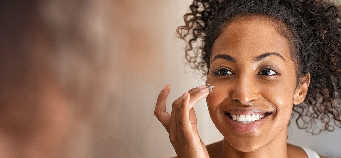woman smiling and applying moisturizer to her cheekbone