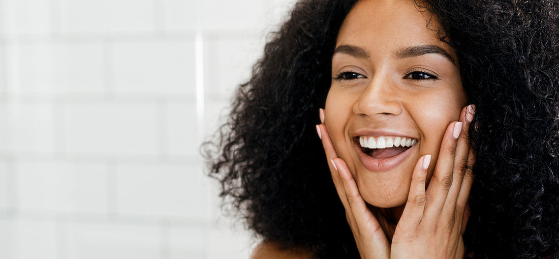 woman looking in the mirror, smiling and holding her cheeks