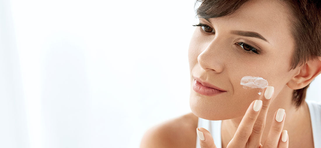 woman applying moisturizer to her cheek in the mirror
