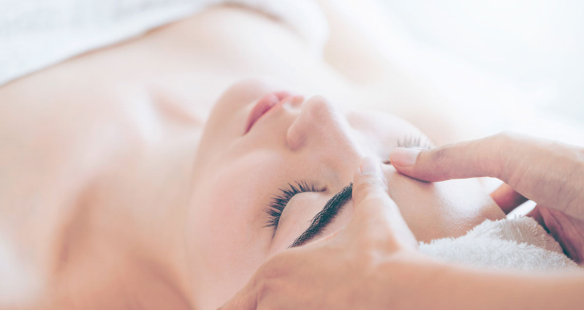 woman on treatment table receiving facial massage from esthetician